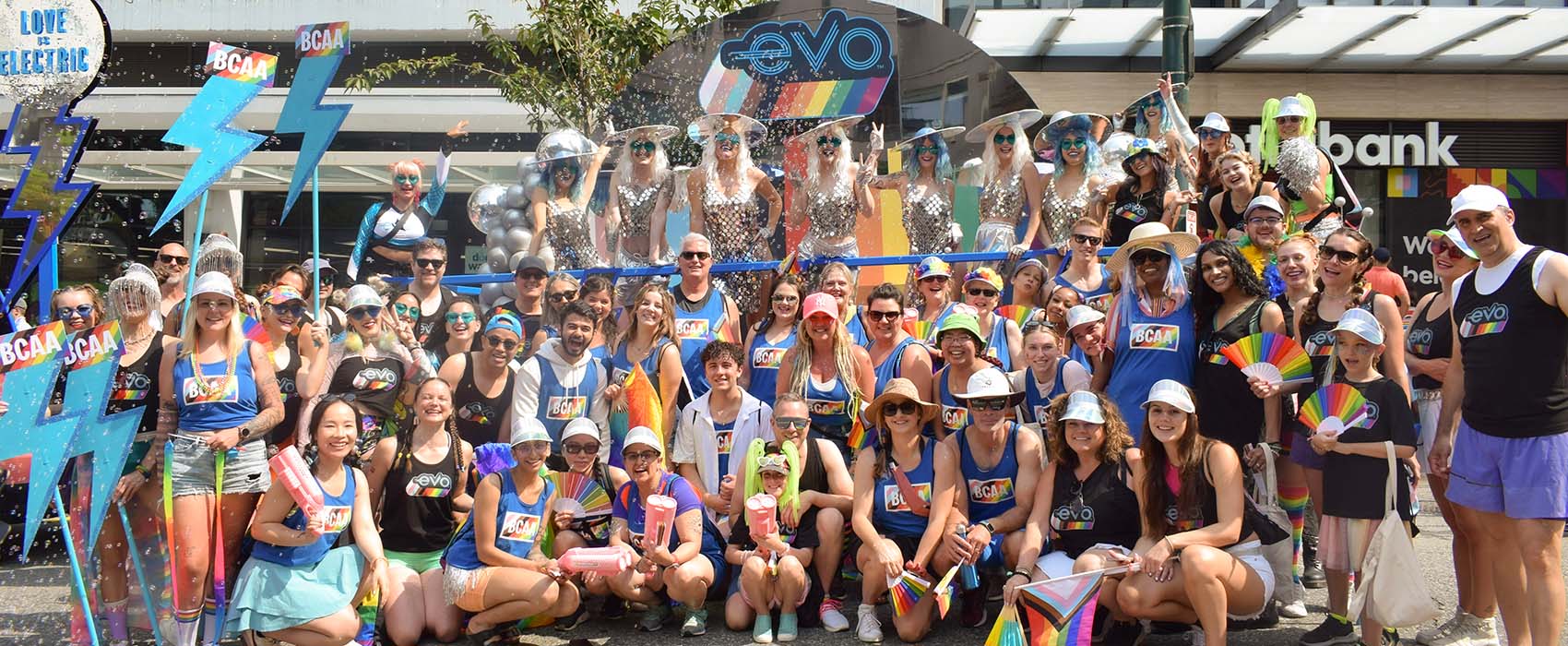 BCAA and Evo employees pose in front of large BCAA and Evo pride parade float