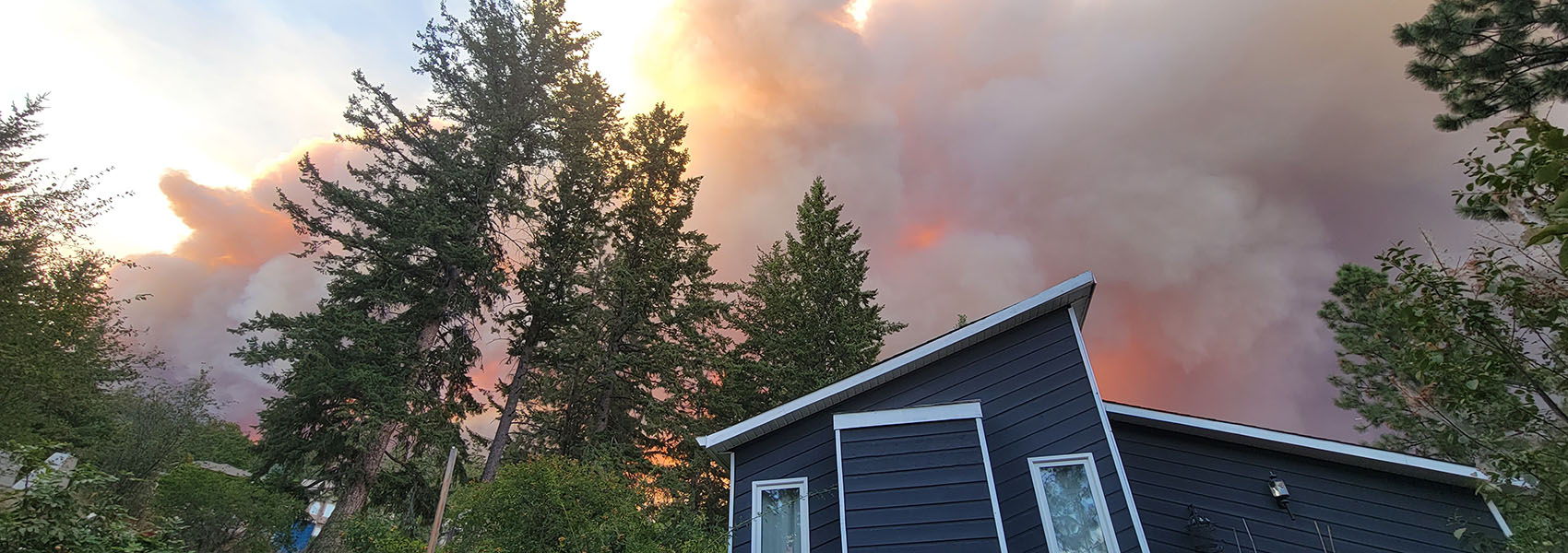 Smoky skies illuminated by wildfire appear over a home in the forest