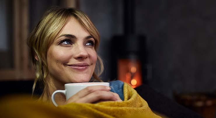 Woman sipping a warm beverage with a fireplace in the background