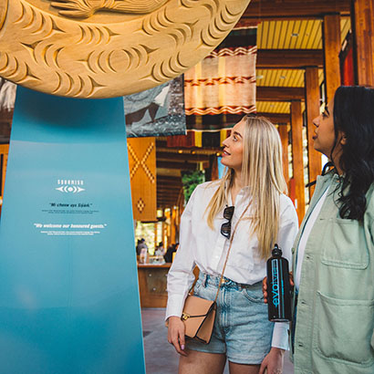 Two women looking at a wooden sculpture at the Squamish Lilwat Cultural Centre